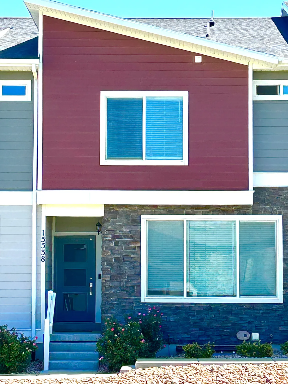 Modern architectural exterior featuring a dark teal entry door with glass inserts, stone veneer, and two-tone siding