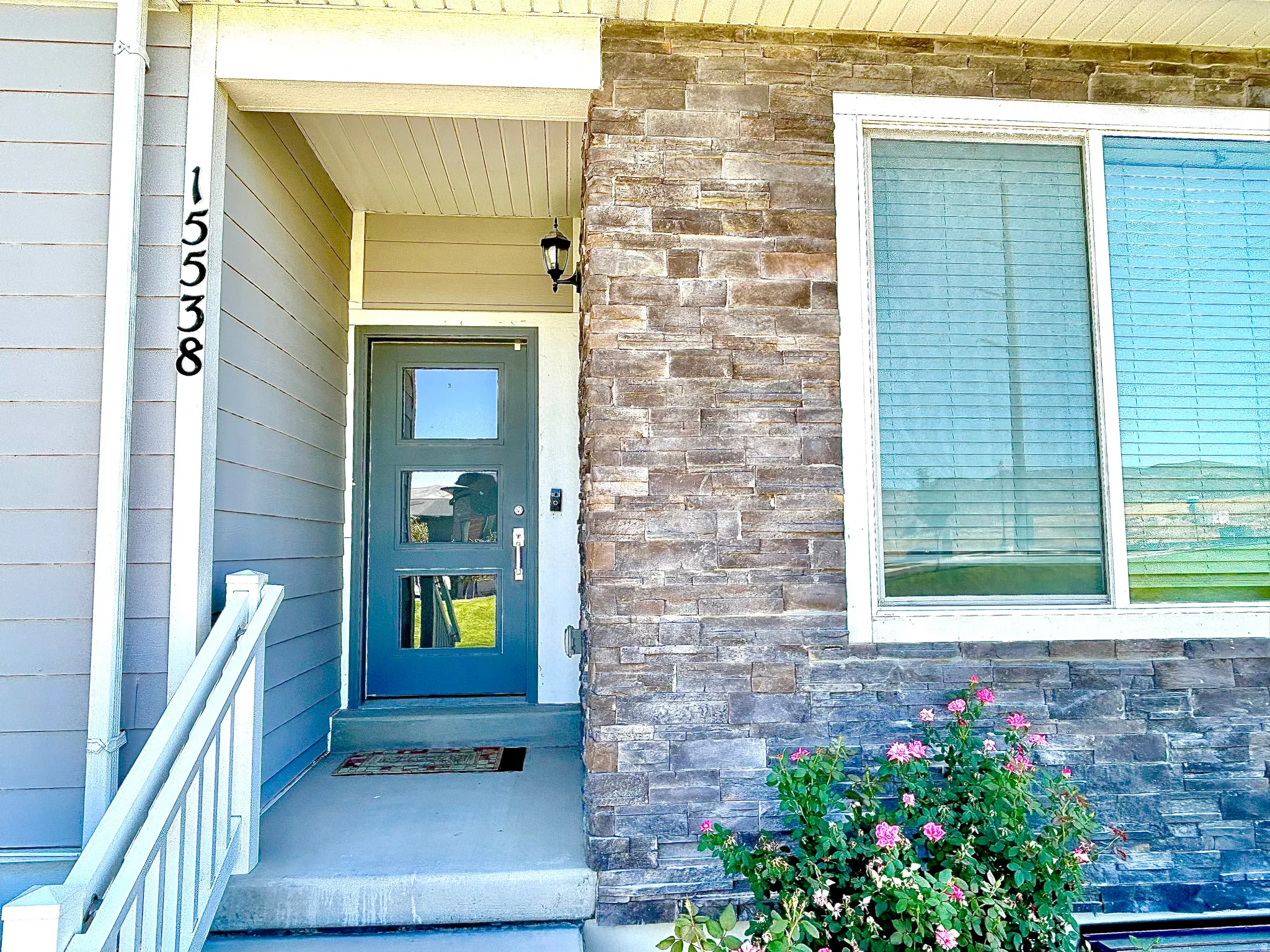 Exterior featuring horizontal siding, stone veneer accents, a contemporary entry door with three glass panes, a white-framed window, and an outdoor wall lantern