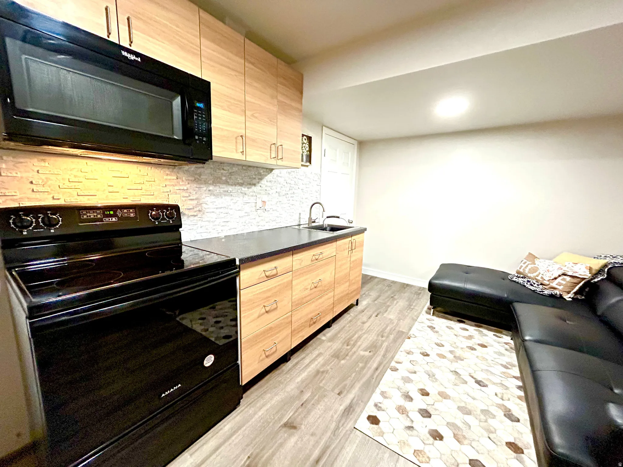 Kitchenette featuring wood-finish cabinetry, black appliances including a built-in microwave and range, dark countertops, and a textured backsplash
