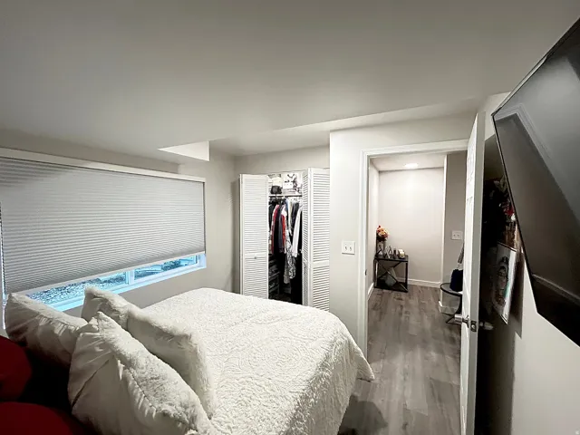 Recessed window with privacy blinds, bi-fold closet doors, and wood-finish flooring