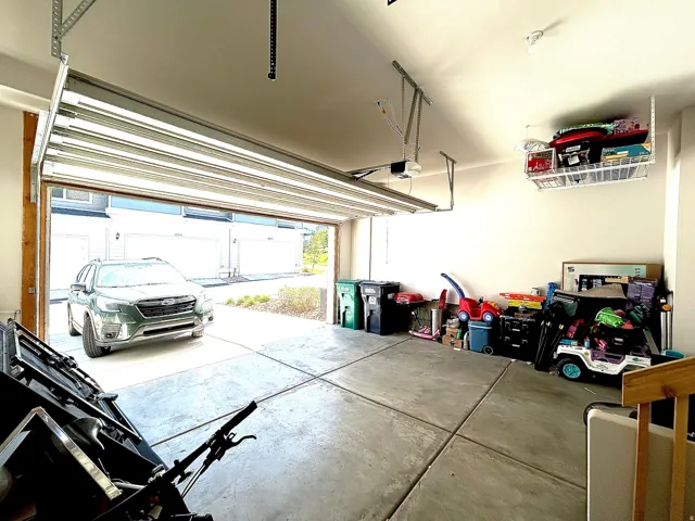 Concrete flooring, white walls, overhead garage door, built-in ceiling storage, and garage door opener