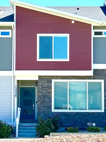 Modern architectural exterior featuring a dark teal entry door with glass inserts, stone veneer, and two-tone siding