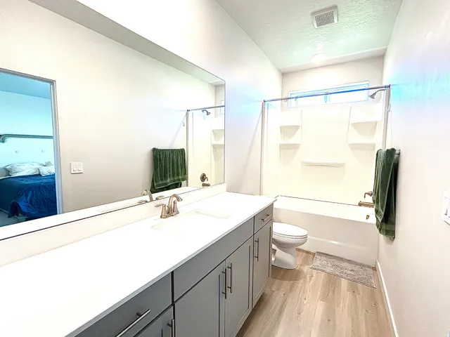 Dual vanity with integrated sinks, light-toned wood-finish flooring, a full-sized bathtub with an overhead shower, a window above the bathtub, and built-in vanity cabinetry