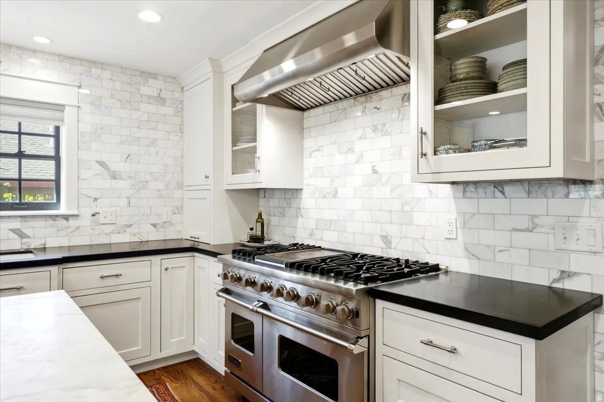 Gourmet kitchen featuring a professional-grade stainless steel range, custom cabinetry, stone countertops, a full-height tile backsplash, and a stainless steel range hood