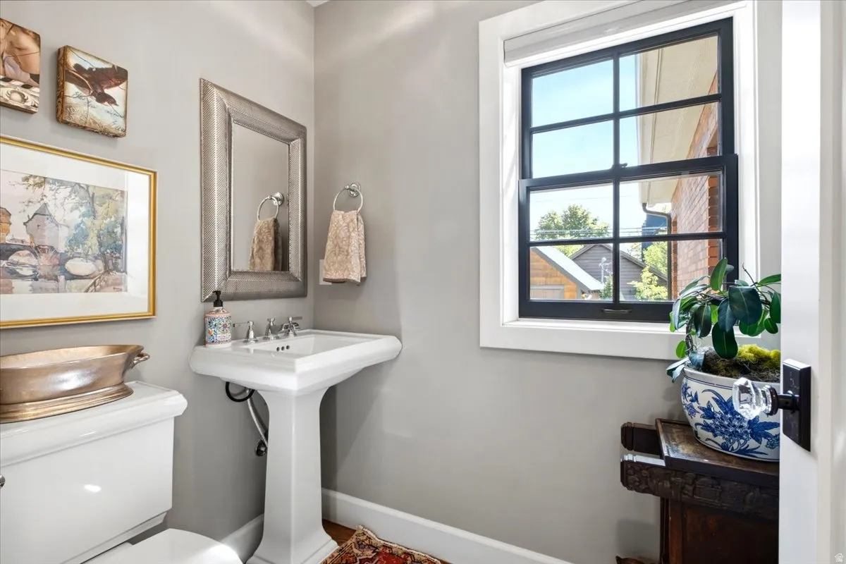 Pedestal sink with chrome fixtures, framed mirror, and a grid-pattern window