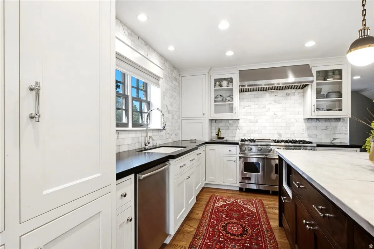 White cabinetry, black countertops, stainless steel appliances, marble tile backsplash, and recessed lighting