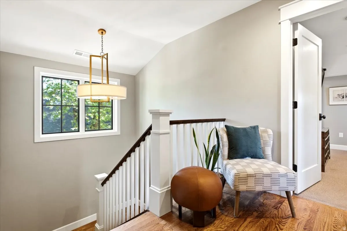 Hardwood flooring, painted white railing with dark wood-finish banister, window with grid pattern, overhead lighting fixture, and white painted interior door