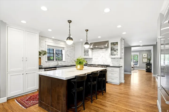 Kitchen featuring a large central island, white cabinetry, a tile backsplash, and wood-finish flooring