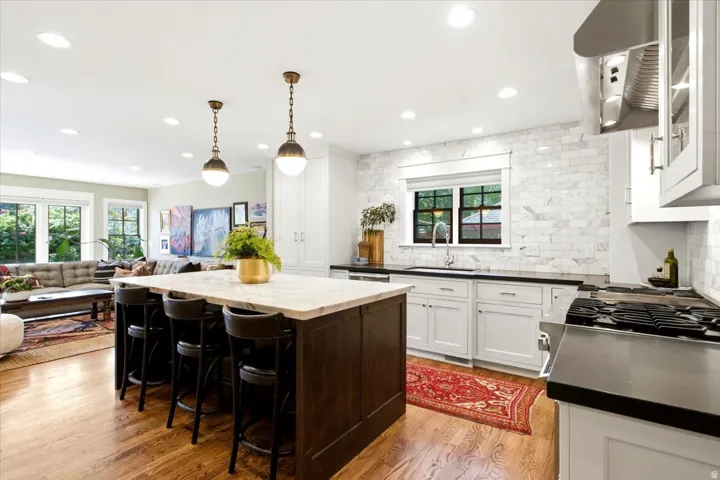 Open-concept kitchen featuring wood-finish flooring, a central island with seating, pendant lighting, stone countertops, and a subway tile backsplash