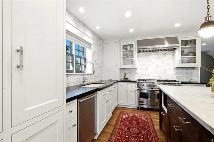 White cabinetry, black countertops, stainless steel appliances, marble tile backsplash, and recessed lighting