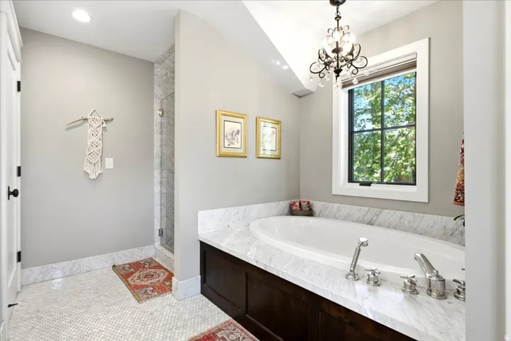 White mosaic tile flooring with a built-in soaking tub featuring a stone surround and dark wood cabinetry