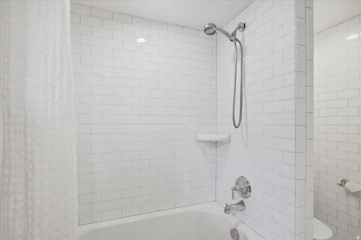 White subway tile surround, polished chrome showerhead, single lever tub/shower faucet, and an integrated shelf