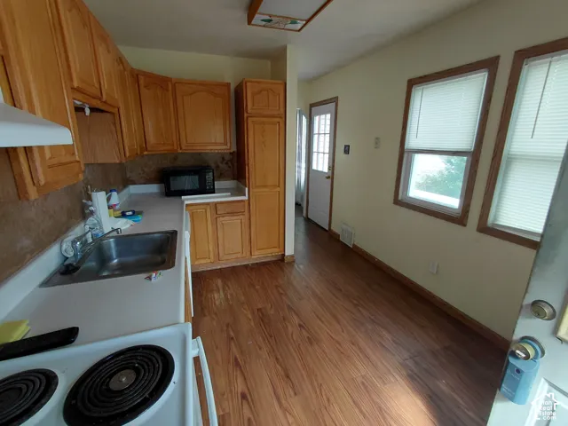 Wood-finish flooring, light wood cabinetry, white countertops, stainless steel sink, and multiple windows with blinds