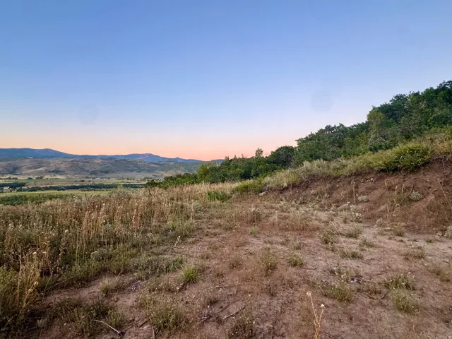 Expansive landscape featuring distant mountains, a valley with green fields, and natural hillside vegetation
