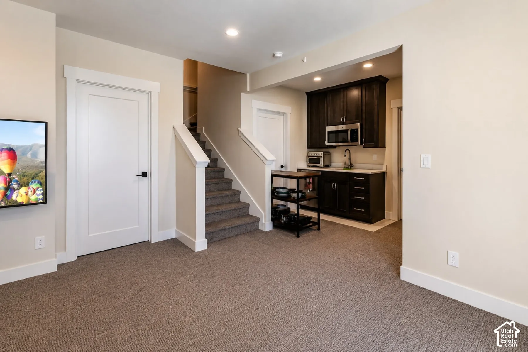 Carpeted flooring, white trim, and a built-in wet bar with dark wood cabinetry and a stainless steel microwave