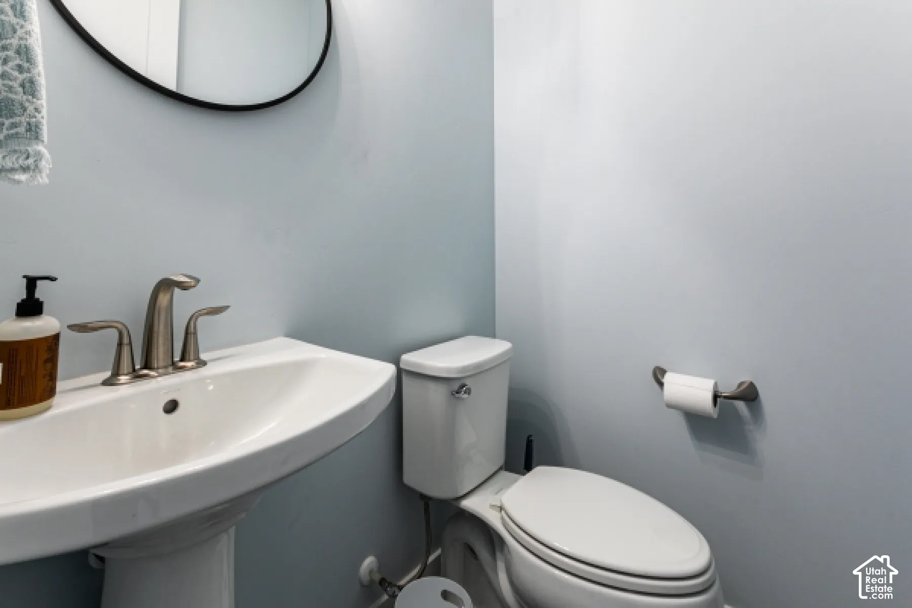 Pedestal sink with brushed nickel faucet, wall-mounted mirror with black frame, and white toilet
