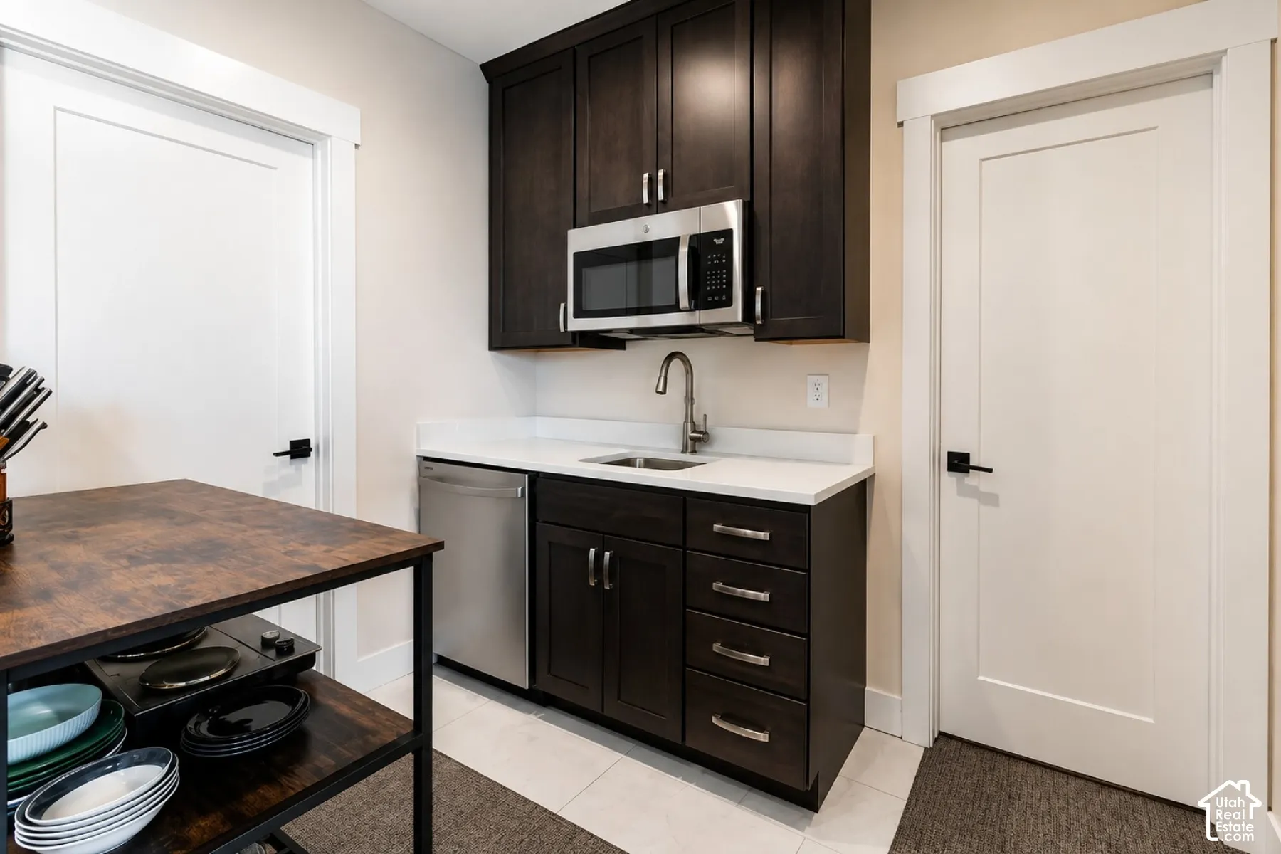 Dark wood-finish cabinetry with stainless steel hardware, white countertop, stainless steel microwave, and white flat-panel doors
