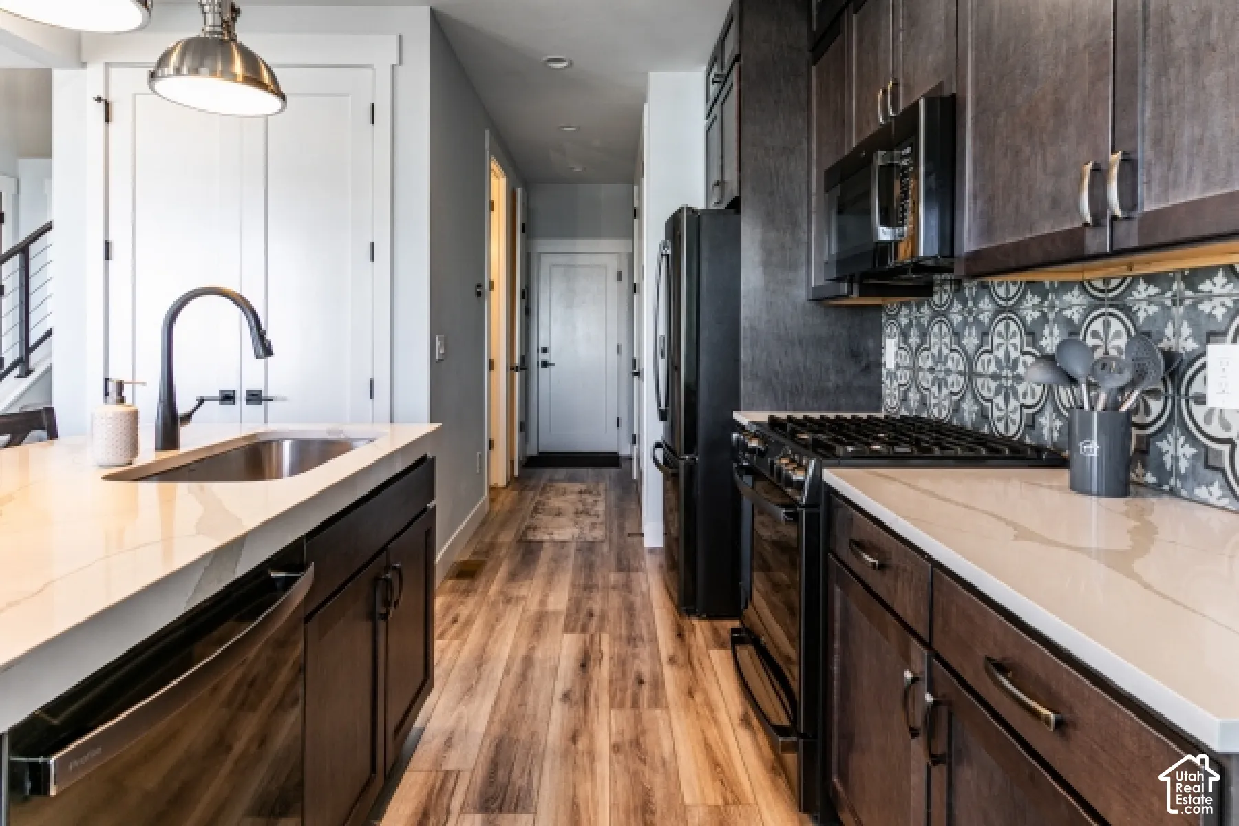 Kitchen featuring wood-finish flooring, dark wood cabinetry, light-toned countertops, a patterned tile backsplash, and stainless steel appliances