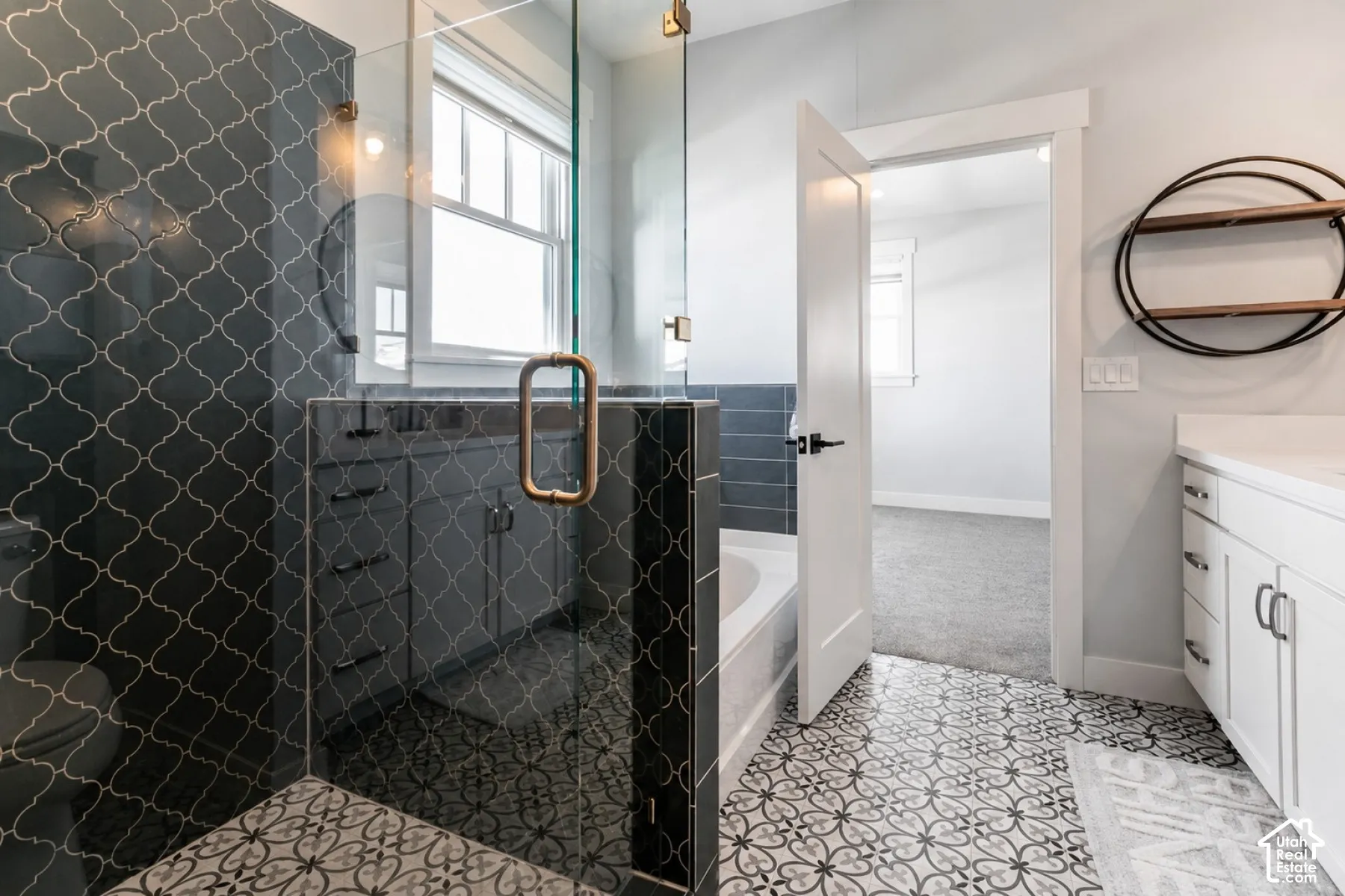 Glass-enclosed shower with arabesque wall tiling, freestanding bathtub, patterned floor tiles, and a white vanity with built-in cabinetry