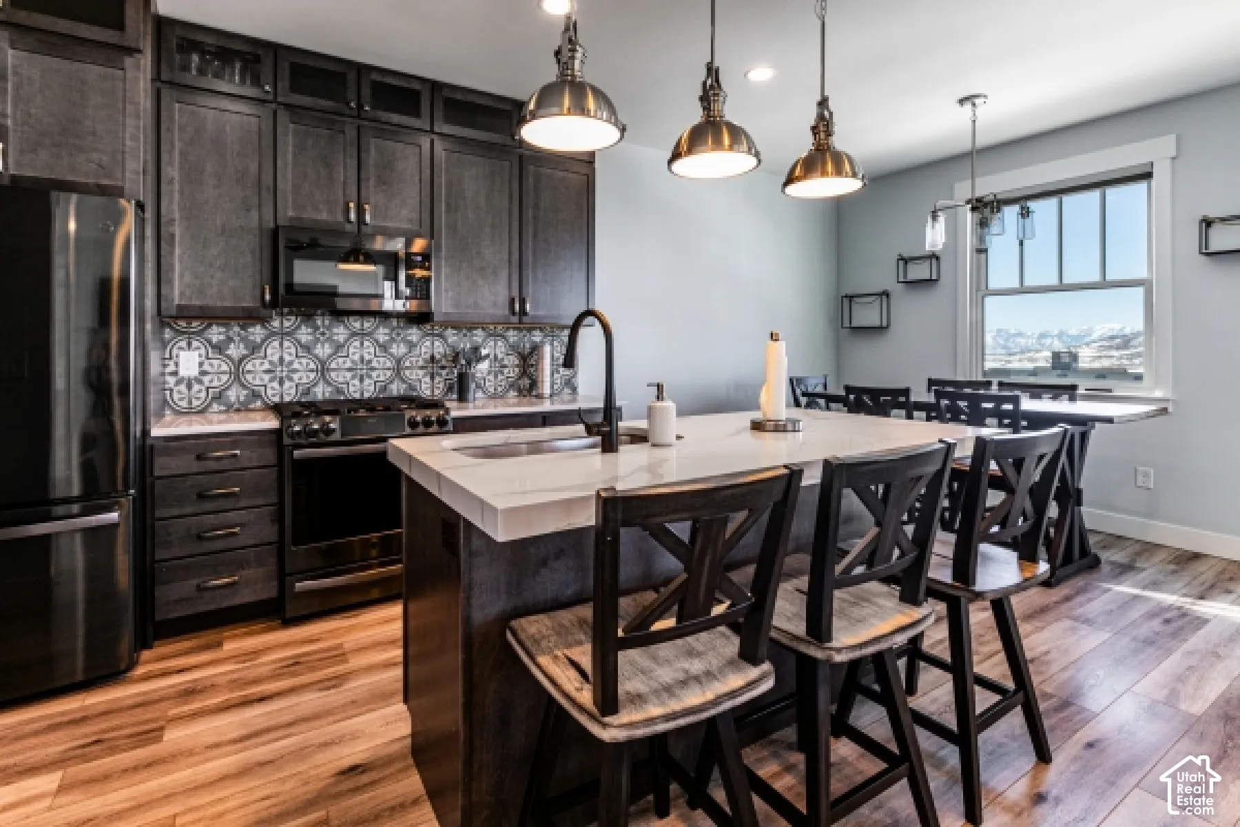 Kitchen featuring dark wood-finish cabinetry, patterned tile backsplash, stainless steel appliances, a center island with countertop seating, and wood-finish flooring