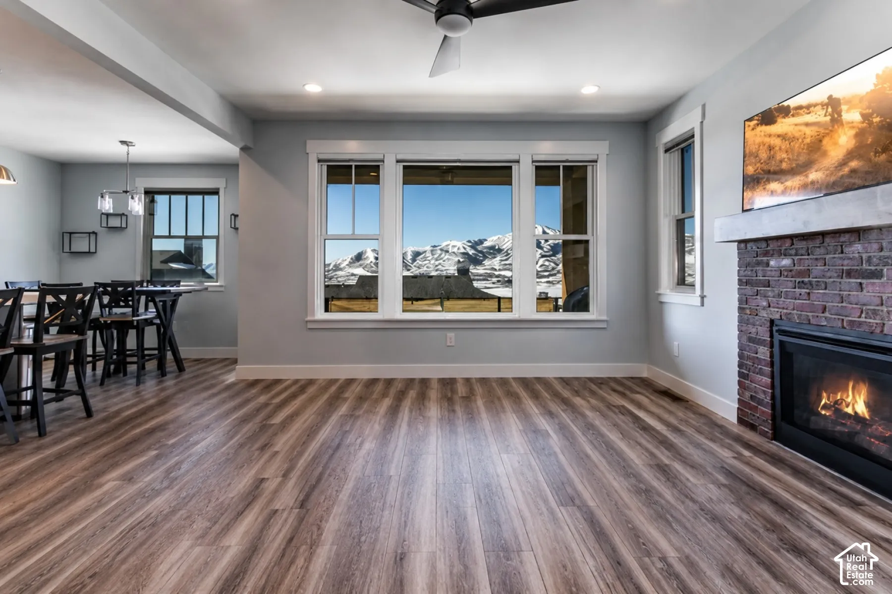 Expansive wood-finish flooring, brick fireplace with a concrete mantel, recessed lighting, and a modern ceiling fan