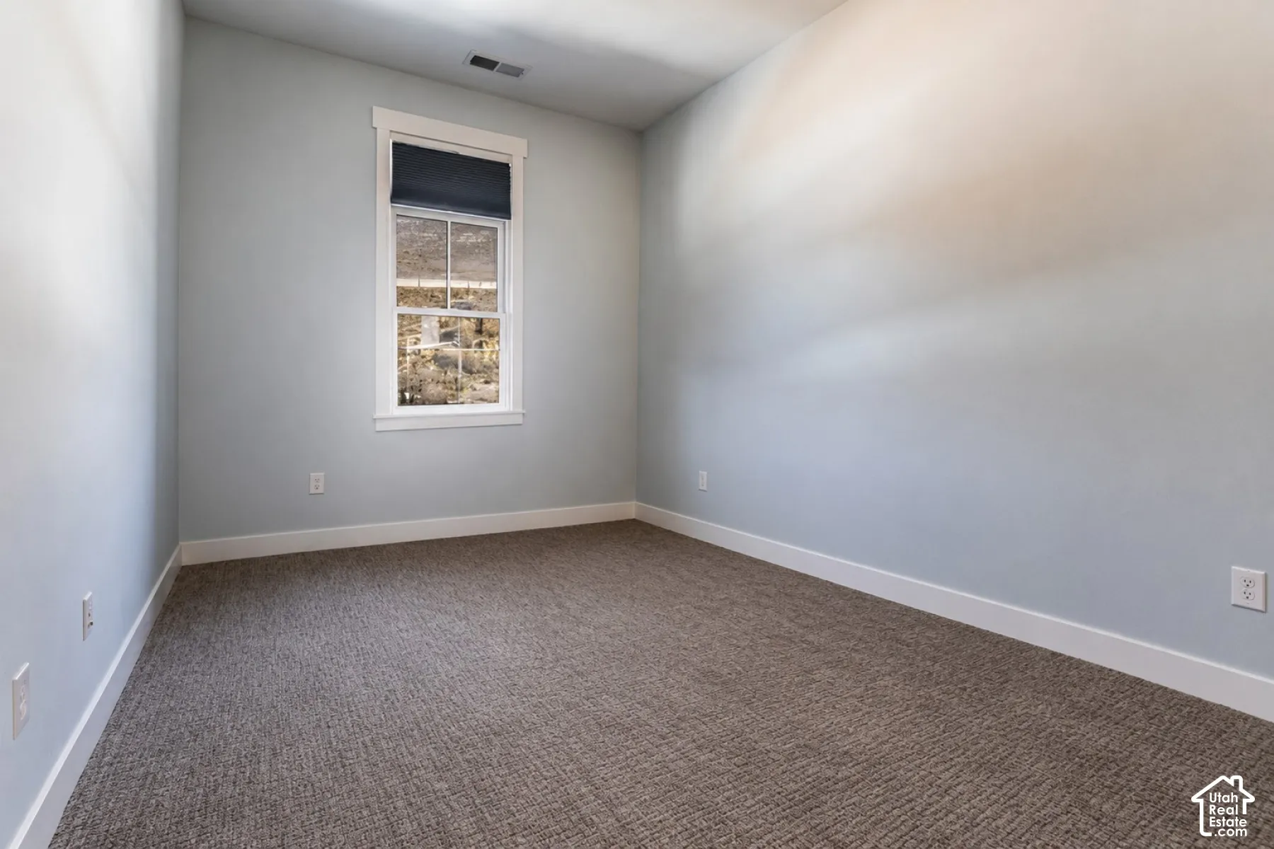 Textured carpet flooring, neutral painted walls, and a single window with a roller shade