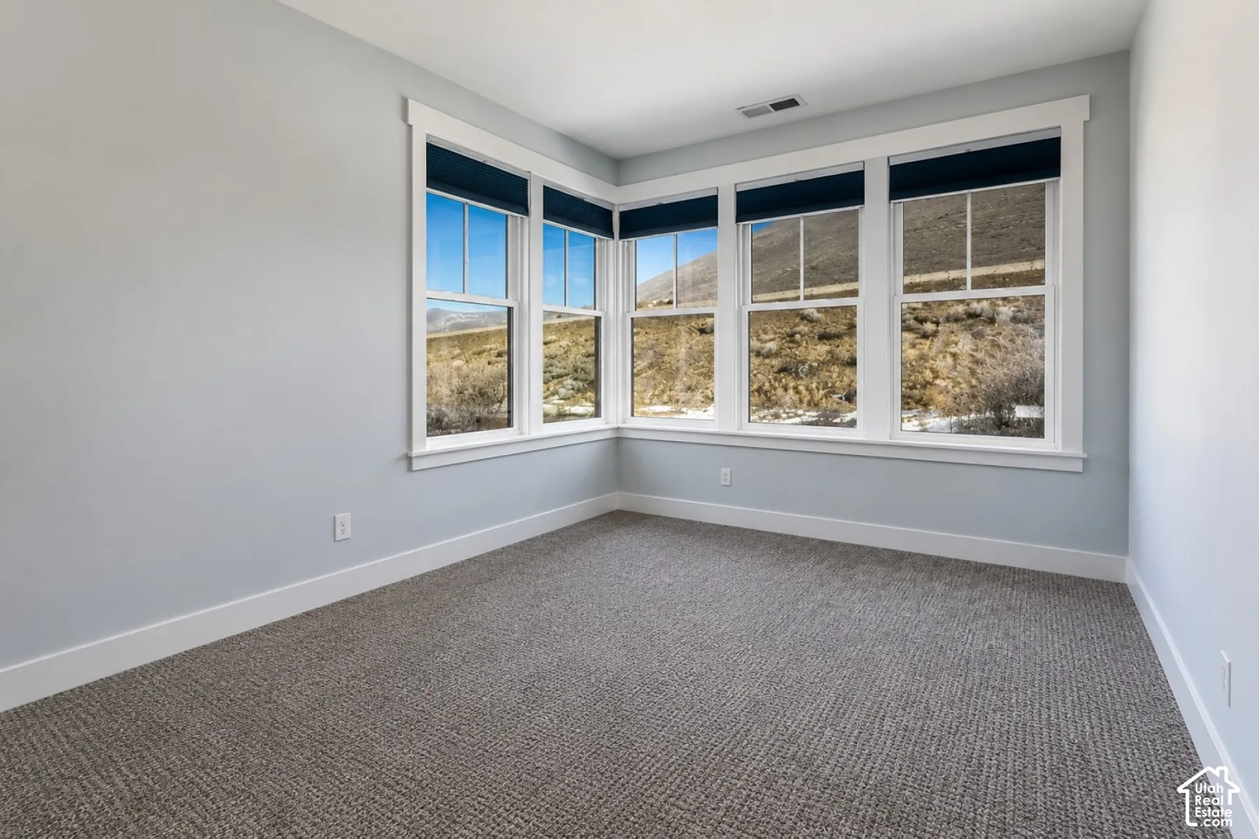 Corner window configuration, gray wall paint, white trim, and gray patterned carpeting
