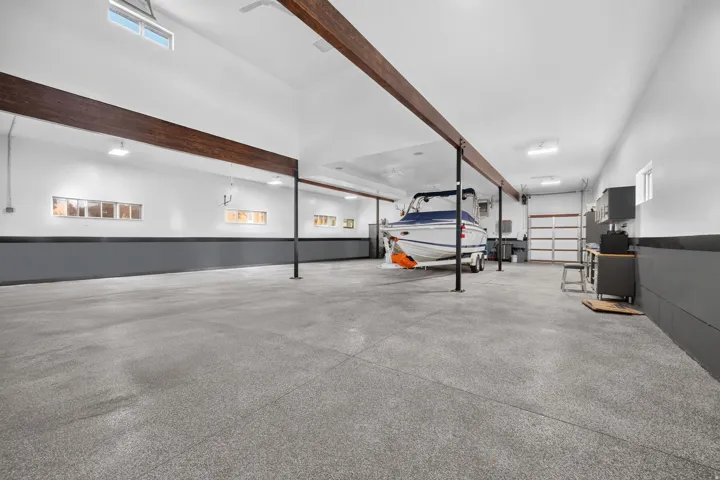 Spacious garage with high ceilings, exposed wood beams, multiple windows, overhead lighting, and an epoxy floor finish