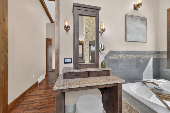 Granite-top vanity with integrated mirror, wood-finish flooring, and a built-in soaking tub