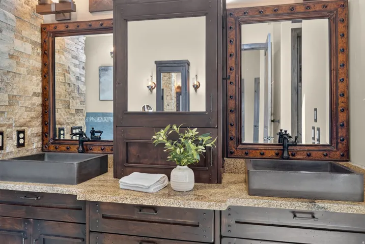Dual rectangular vessel sinks, rustic wood-framed mirrors, a stone veneer accent wall, and a light-toned countertop