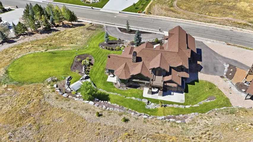 Multi-level architectural design with a brown shingle roof, integrated outdoor patio, and a landscaped yard featuring a rock garden