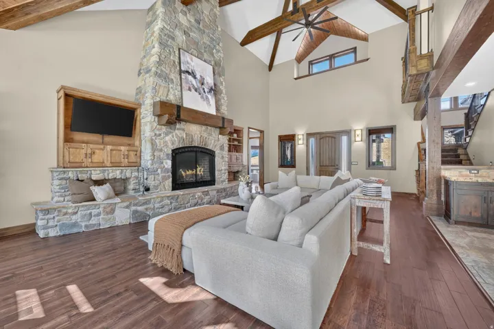 Vaulted ceilings with exposed wood beams, a stone fireplace with a built-in hearth, wood-finish flooring, and a built-in media cabinet