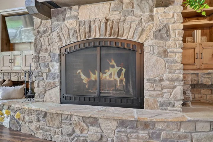 Stone-clad fireplace with arched firebox and metal screen