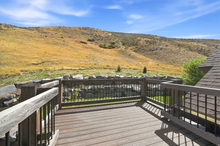 Expansive outdoor deck with composite decking and dark railings, featuring a rock retaining wall and sloped terrain in the background