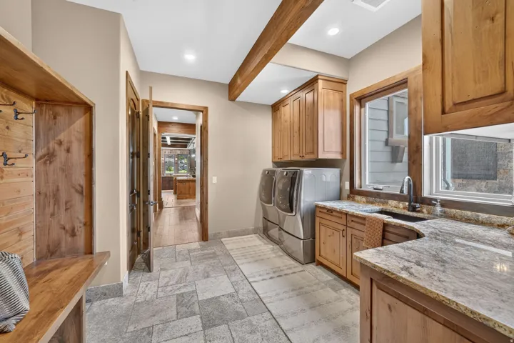 Built-in wood-paneled bench with coat hooks, stone tile flooring, wood cabinetry with stone countertops, and a built-in sink with a gooseneck faucet