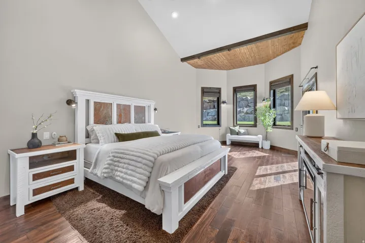 Vaulted ceiling with wood-paneled accent, wood-finish flooring, three windows with dark trim, and sconce lighting