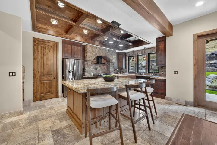Kitchen featuring a wood-beam coffered ceiling, stainless steel refrigerator, stone arch over the range, wood-finish cabinetry, and a granite-top island
