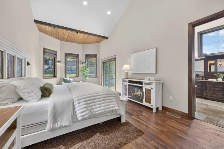 Vaulted ceiling with wood-finish accent, multiple windows, wood-finish flooring, and a built-in electric fireplace