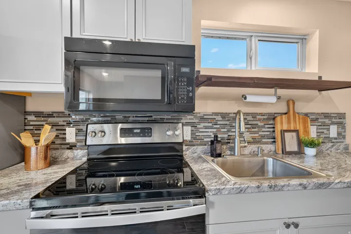 Stainless steel range and microwave, mosaic tile backsplash, stainless steel sink, and wood-finish open shelving