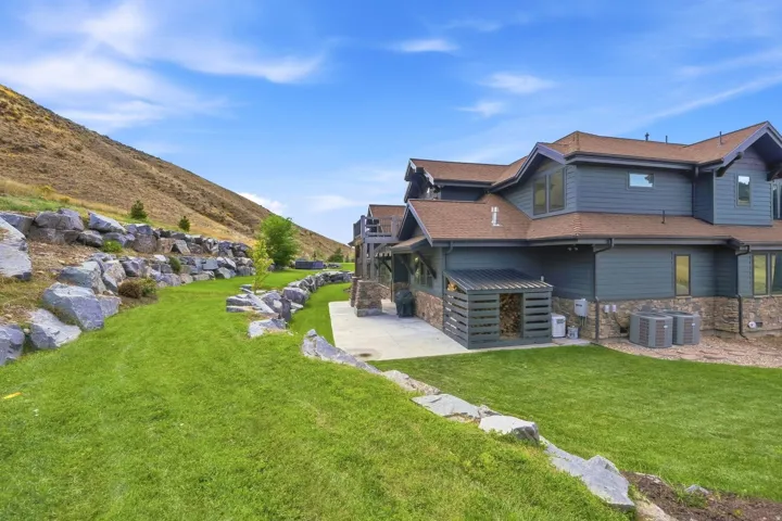 Stone retaining walls framing a green lawn, a hillside backdrop, exterior siding, and a concrete patio