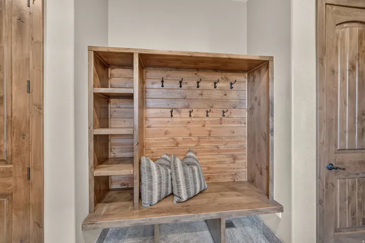 Built-in wooden mudroom bench with integrated shelving and wall-mounted hooks, complemented by natural wood-finish doors