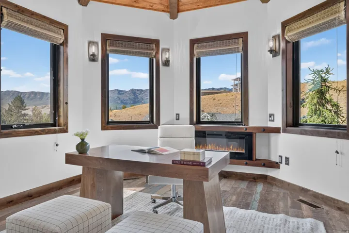 Corner room featuring multiple windows with wood-finish trim, a built-in linear electric fireplace, wood-finish flooring, and exposed wood ceiling beams