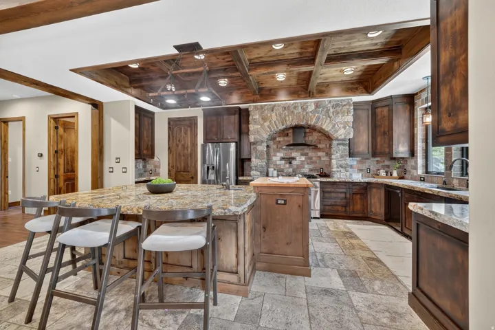 Kitchen featuring a large island with granite countertops, wood cabinetry, a stone accent wall, stainless steel appliances, and a wood-paneled ceiling with recessed lighting