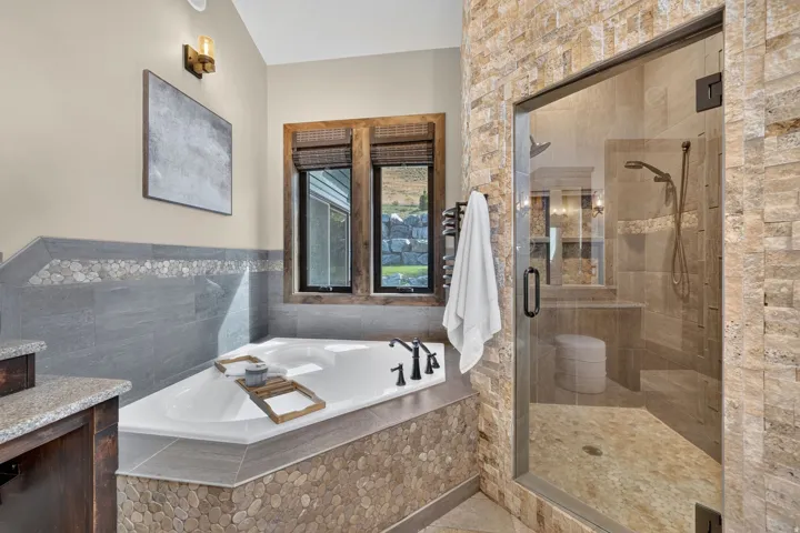 Corner soaking tub, dual windows with wood trim, walk-in shower with glass enclosure, tiled shower walls, and a built-in shower bench
