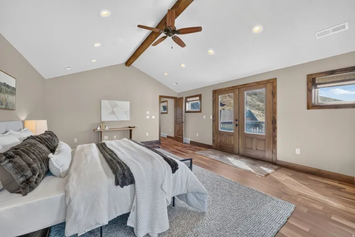 Vaulted ceiling with exposed wood beam, recessed lighting, wood-finish flooring, and double French doors with wood trim