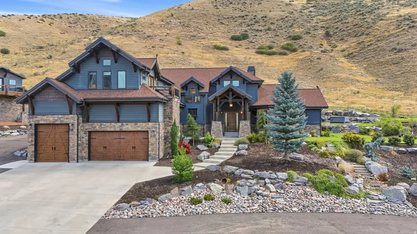 Craftsman-style exterior with stone and siding facade, covered front entry, attached multi-car garage with wood-finish doors, and extensive rock landscaping