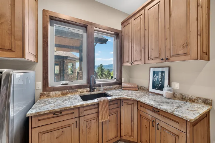 Wood-finish cabinetry with dark hardware, L-shaped countertop, undermount sink with a dark-finish faucet, and window with wood-finish trim