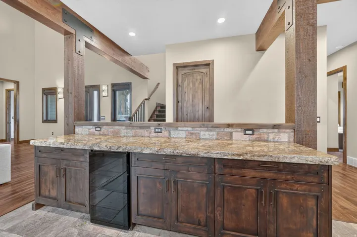 Built-in bar with wood-finish cabinetry, stone-finish countertop, and tile backsplash