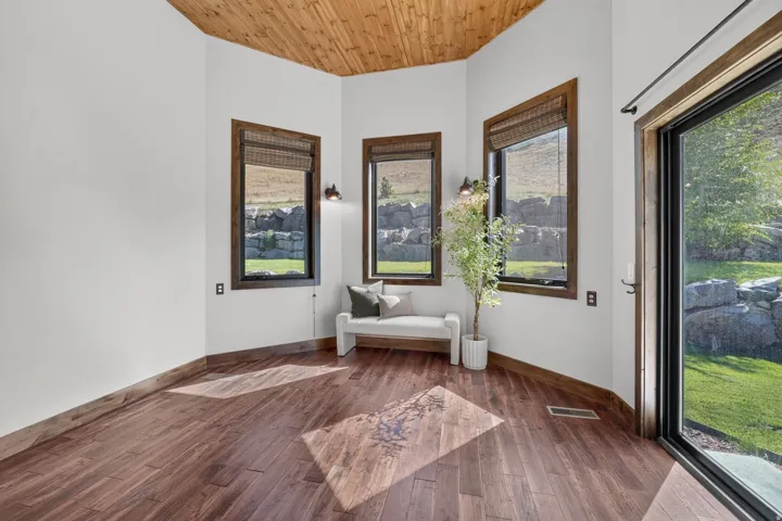 Wood-finish flooring, wood-paneled ceiling, multiple windows with dark frames, and a glass-paneled exterior door