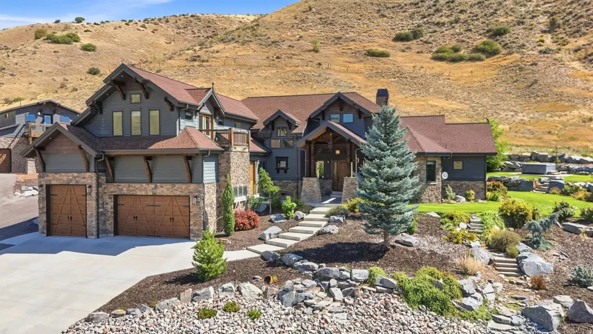 Multi-level residence featuring stone and siding exterior, a multi-car garage with wood-finish doors, and extensive landscaping with natural rock and mature trees